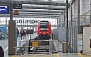 In der rechten Bildhäfte ist ein Stück Baustellenzaun als Absperrung zum Bahnsteig von Gleis 26 erkennbar. In der Mitte Gleis 25 mit einem roten Zug von DB Regio. Links der Bahnsteig zu Gleis 24/25.
