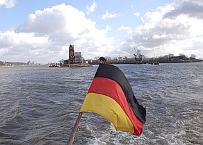 Elbblick bei Finkenwerder mit Heckflagge des Schiffs 
(Bundesflagge), im Hintergrund Backsteingebäde mit Uhrenturm, in der Ferne Hamburg