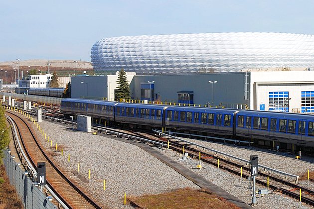 U-Bahn-Zug in Fröttmaning, dahinter Werkstatthalle und Fußballarena