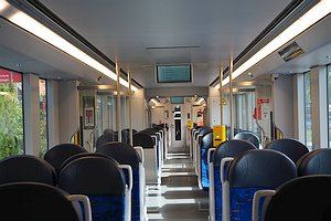 Blick durch den Zug, blau gemusterte Sitze, Informationsanzeige als Deckengondel, gelbe Ticketentwerter.