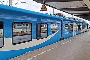 Blau-weißer Zug steht am Bahnsteig, die Aufschrift Arverio ist zu erkennen, in den Fenstern spiegeln sich weitere Züge