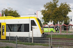 gelb-weißer Zug (vorderer Teil Regio-Shuttle) im bwegt-Design und im Hintergrund ein grüner Flixbus