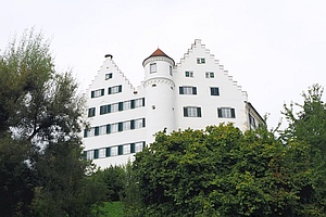 weißes Schlossgebäude mit Turm und gestuften Giebeln auf einem Hügel