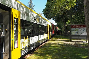 Zug in Seitenansicht, gelb-weißer Teil vorne, roter Teil hinten (jeweils Regio-Shuttle) rechts Bäme und ein Schild 'Pfullendorf'